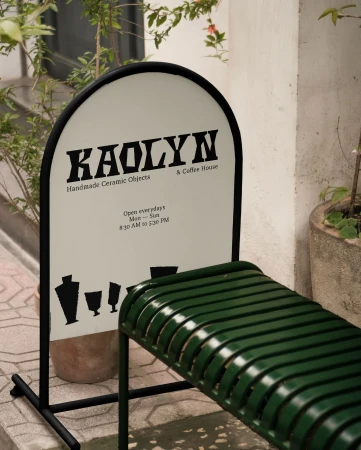Kaolyn sign with handmade ceramic objects and coffee house advertisement, accompanied by an outdoor green metal bench.