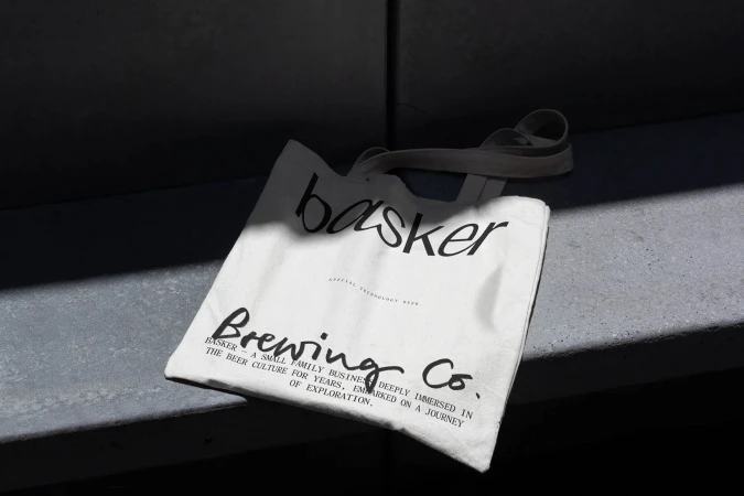 Canvas tote bag with 'basker Brewing Co.' text, branding for a small family business deeply immersed in beer culture on grey surface.