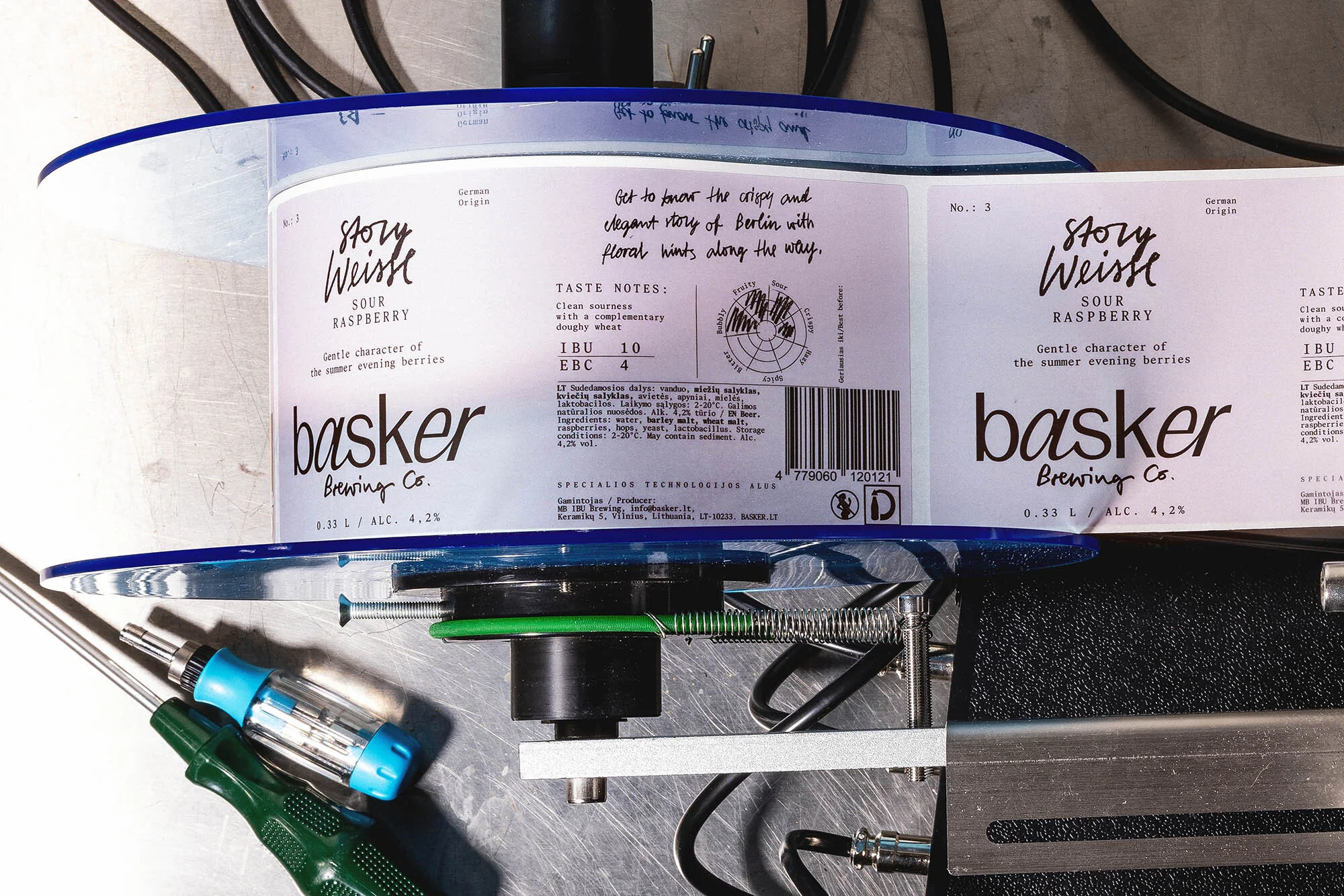 Craft beer labels for Basker Brewing Co. featuring the Story Weisse Sour Raspberry variety, displayed on a label application machine.