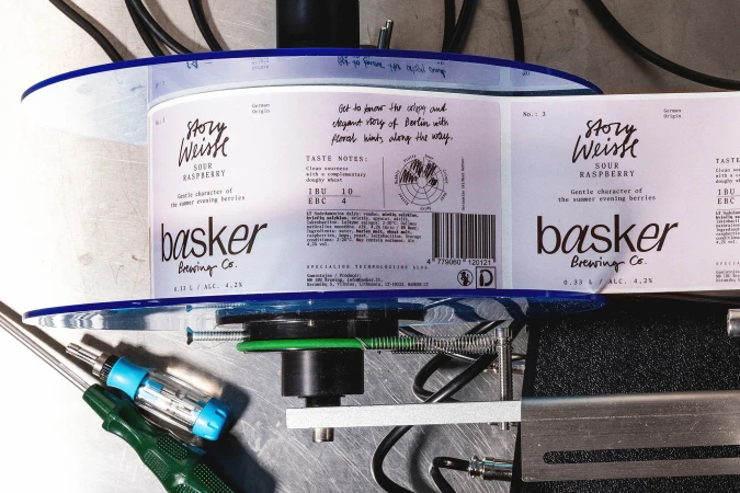 Craft beer labels for Basker Brewing Co. featuring the Story Weisse Sour Raspberry variety, displayed on a label application machine.