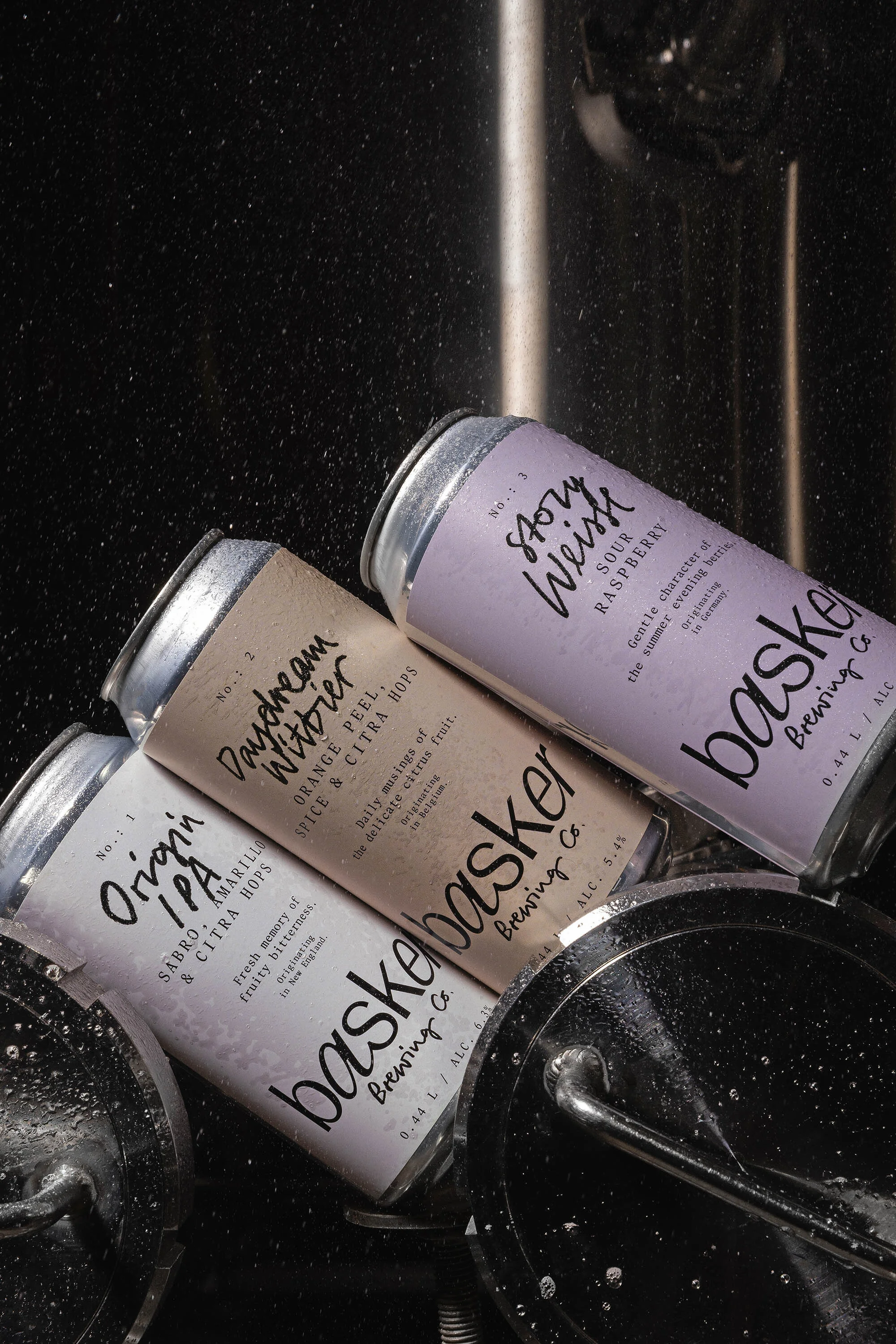 Three Basker Brewing Co. cans: Origin IPA, Daydream Witbier, Story Weisse Sour Raspberry, showing the labels with brand names on metal lids.