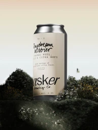 An aluminium beverage can with cream label set among dark mossy mounds and small flowers against a warm gradient sky.