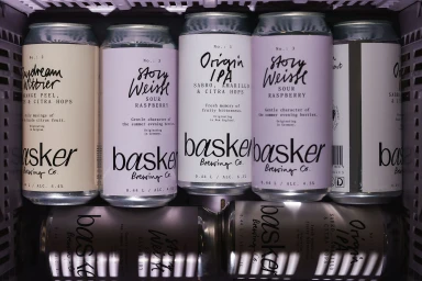 Top-down view of six tall beverage cans with minimalist labels and typography arranged neatly inside a dark crate.