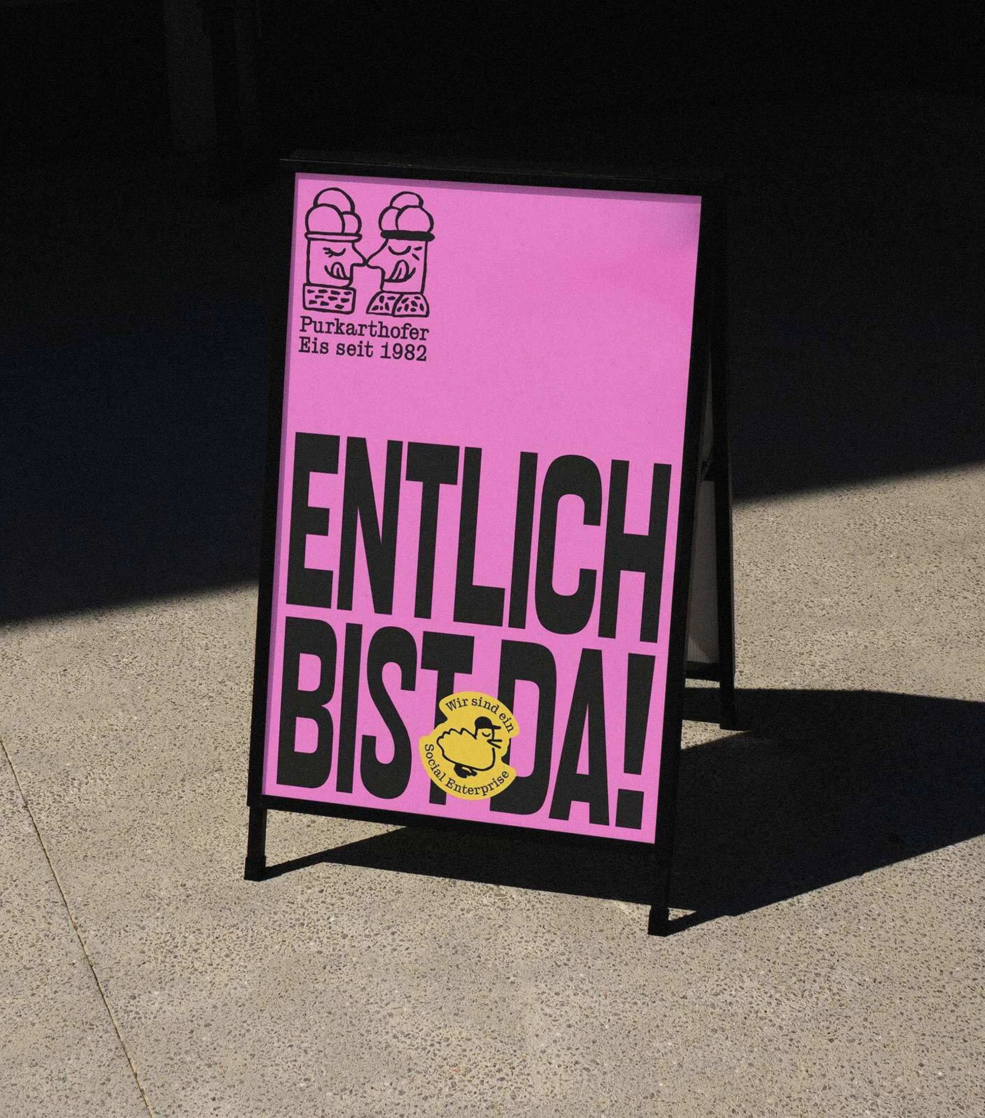 A-frame sidewalk sign features a pink poster for Purkarthofer ice cream with the text 'Endlich bist du da!' and cartoon ice cream cones.