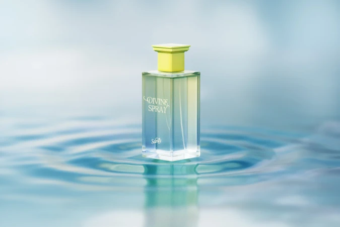 Elegant square perfume bottle with yellow cap on reflective water surface, soft blue background, beauty product advertising.