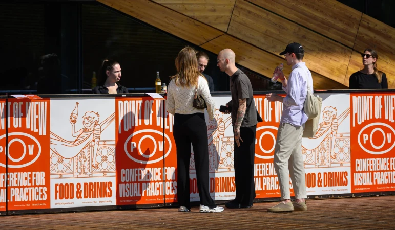 Several people stand near an outdoor promotional display for a food and drink conference; sunny outdoor setting.
