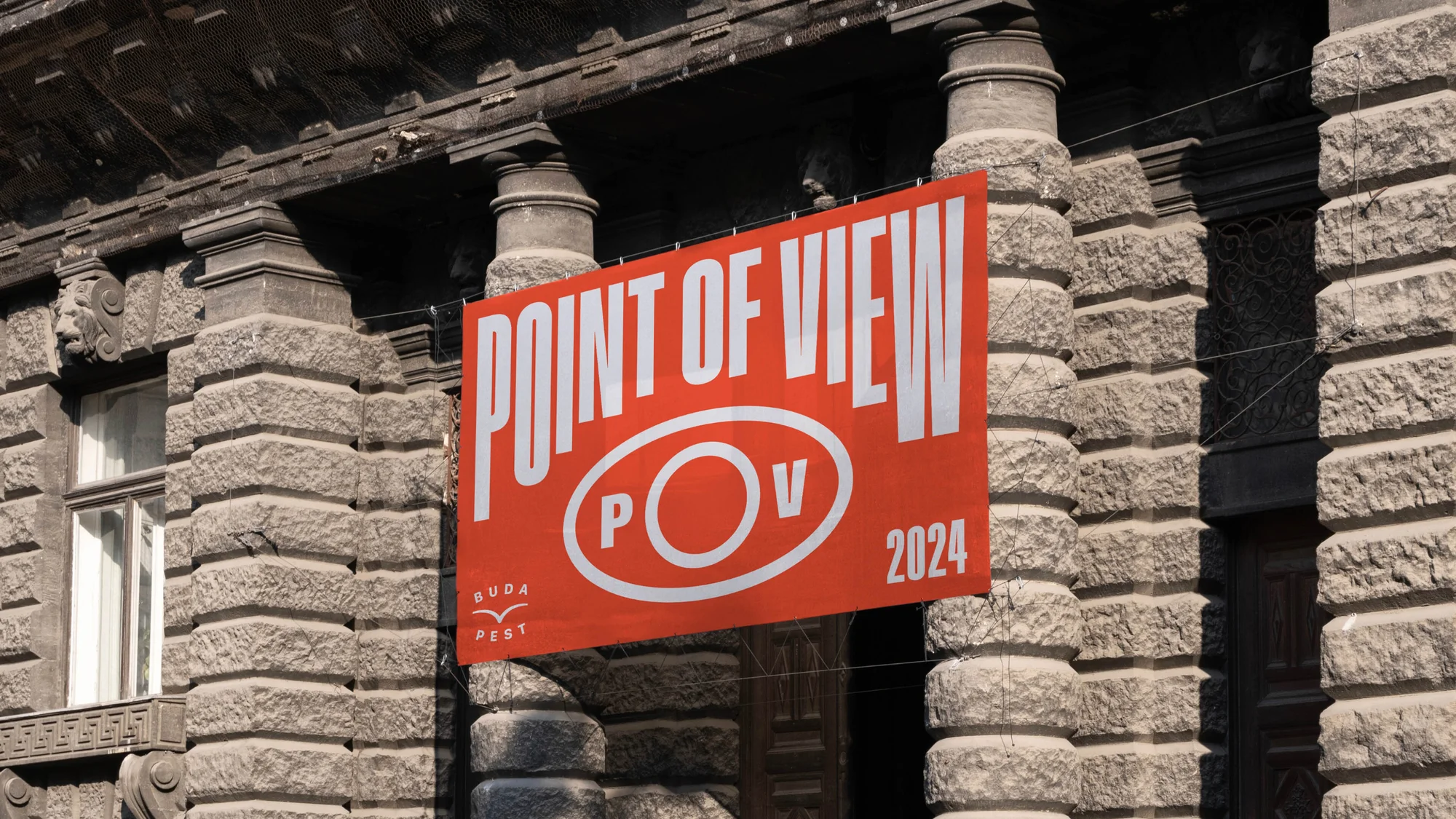 Banner for Point of View (POV) festival in Budapest, Hungary, hanging on an ornate stone building with architectural details.