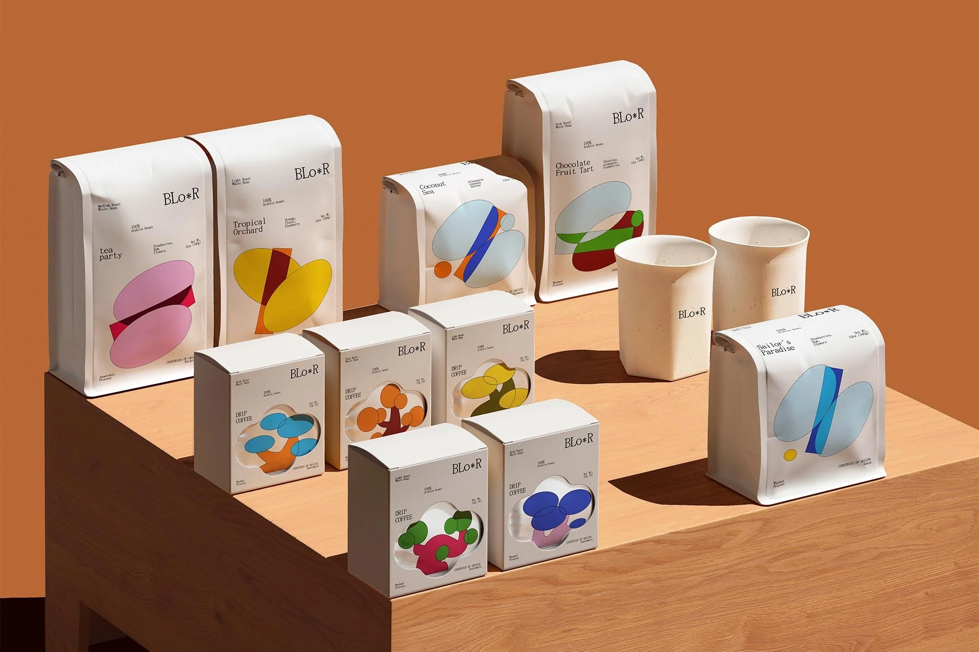Assortment of Blo-R coffee products including bags and boxes, displayed on a wooden surface against a warm orange background.