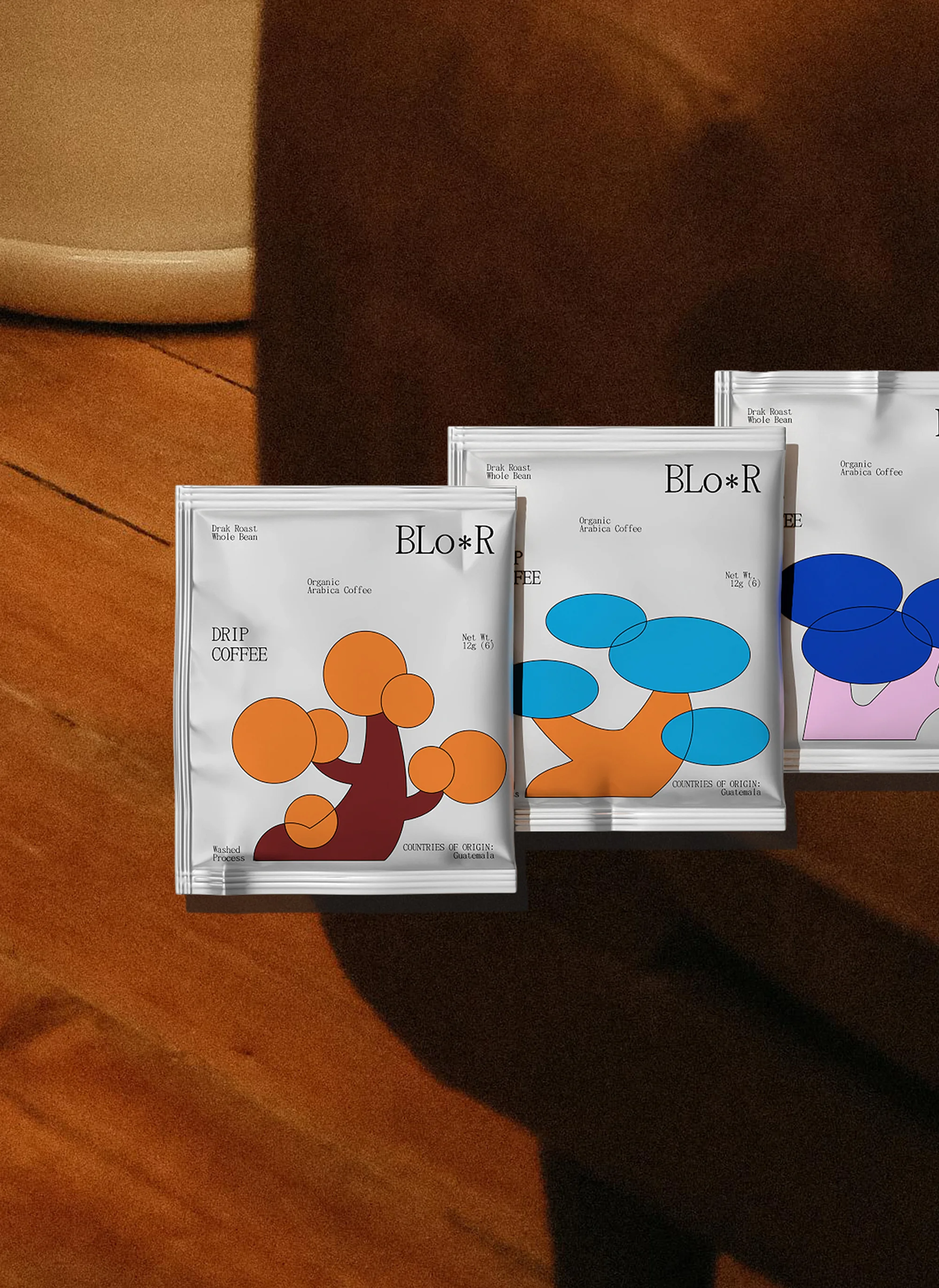 Close-up of Bloor Drip Coffee packets with graphic designs against a warm wooden surface and soft studio lighting, modern branding.