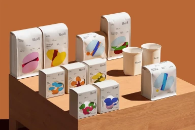 Collection of white branded product packaging boxes and bags with colorful geometric graphics displayed on a wooden pedestal.
