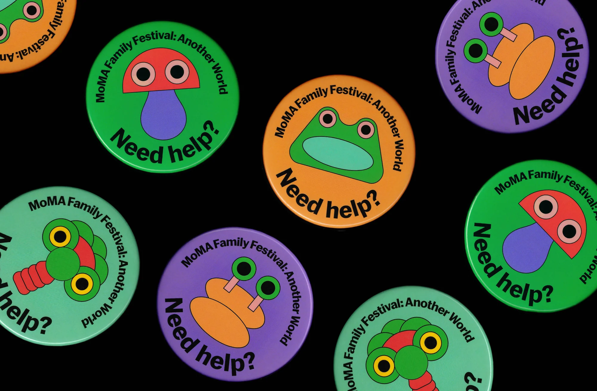Colorful MoMA Family Festival buttons display whimsical cartoon creatures and the question, 'Need help?' over a stark black background.