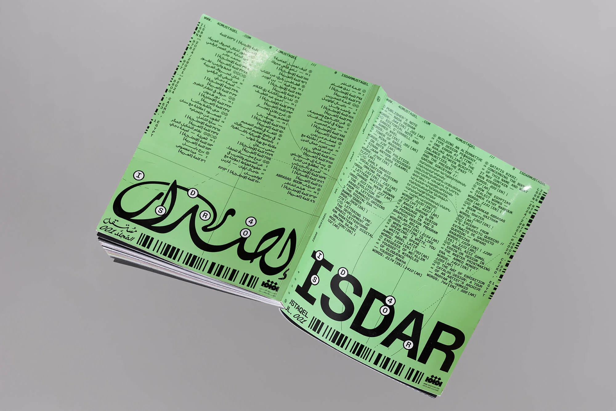 Opened magazine with Arabic and English text on a green background, featuring a barcode-like design element for modern visual appeal.