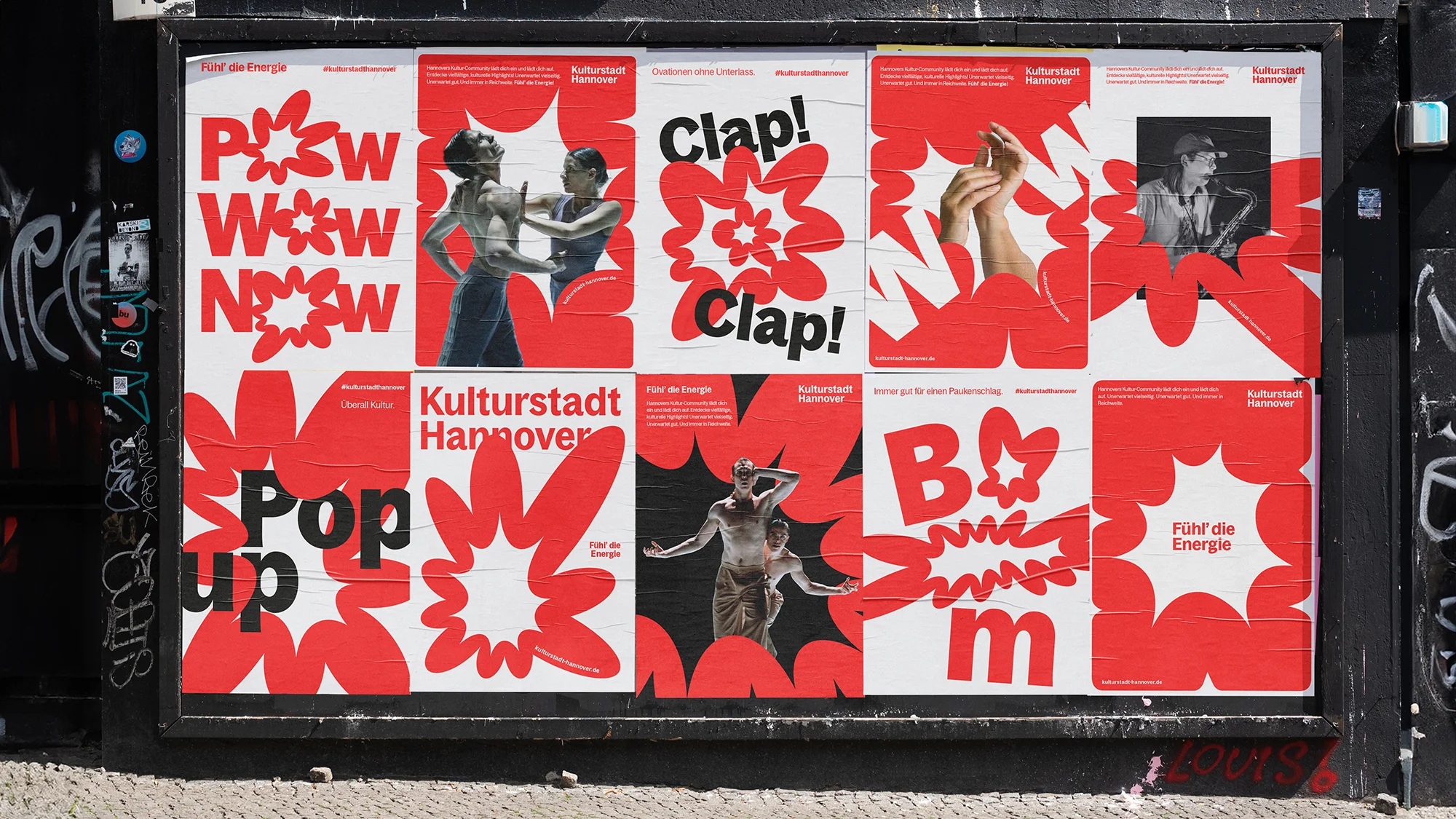 Outdoor advertisement on a black bulletin board features red and white graphic posters promoting 'Kulturstadt Hannover' with visual art.