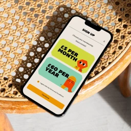 Smartphone displaying a membership sign up screen resting on a round woven rattan stool surface
