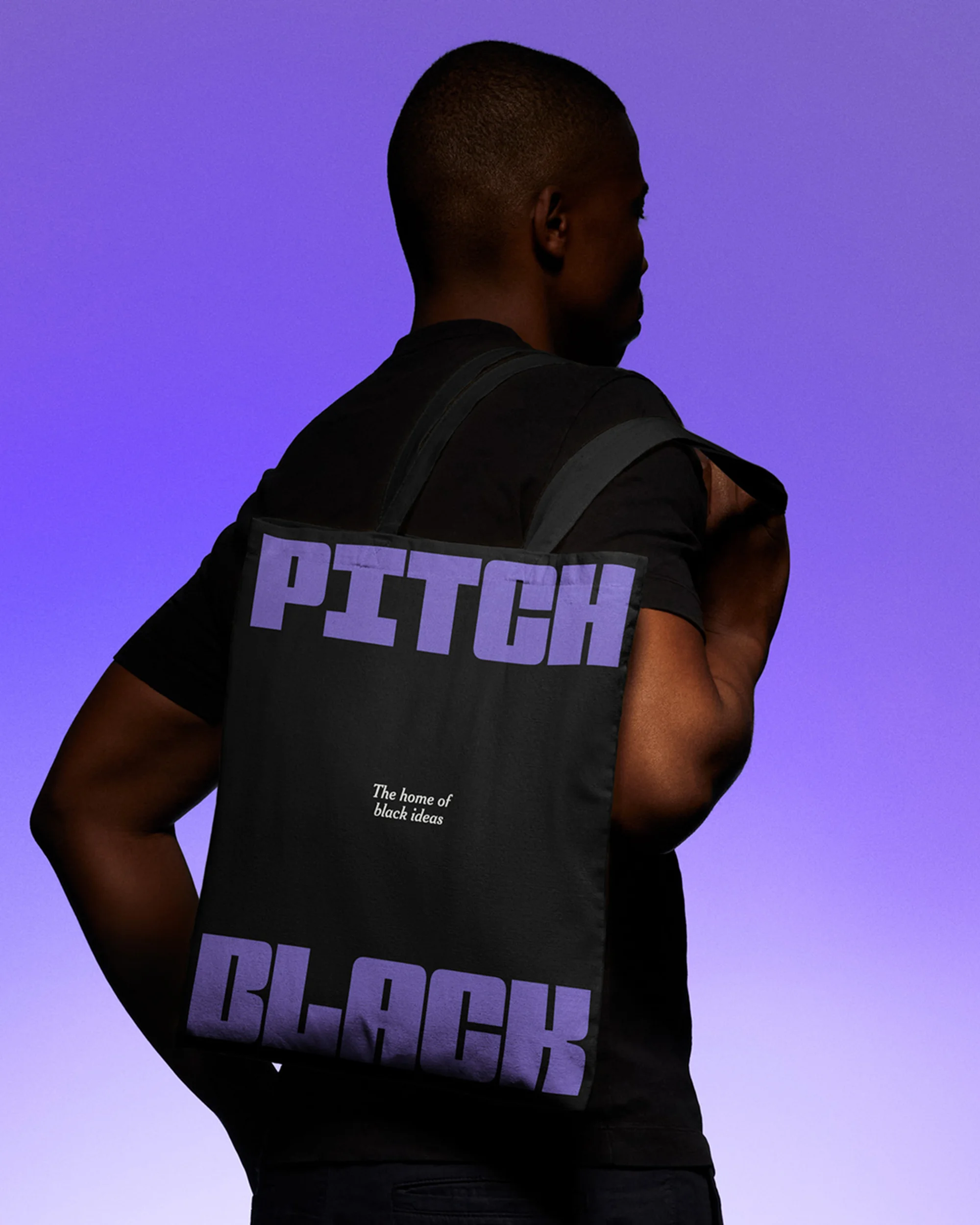 Man with a black tote bag over his shoulder, 'Pitch Black' printed on it in violet letters, against a purple gradient background.
