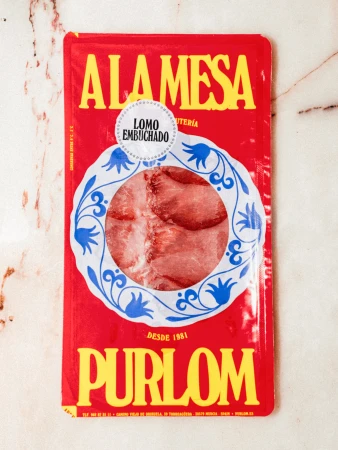 Packaged cured pork loin on a marble surface featuring the brand 'Alamesa' in yellow lettering on a bright red package.