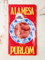 Red packaged sliced cured meat product with yellow typography and white decorative plate graphic on marble surface