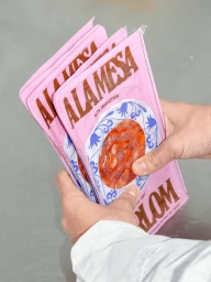 Person holding several pink packaged food items featuring brown typography against a neutral grey surface