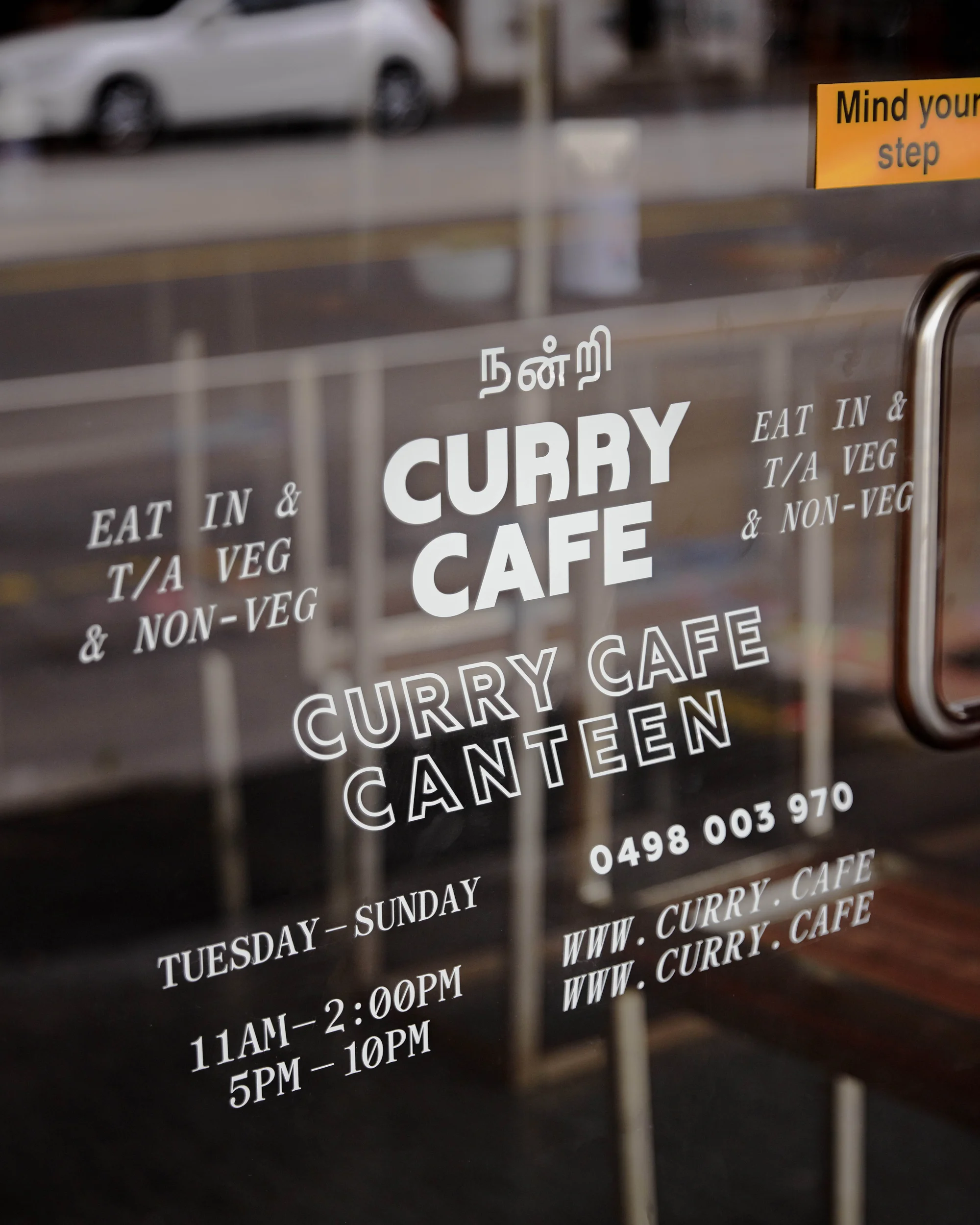 Curry Cafe sign on window. Restaurant hours and contact information are listed, along with information about eat in and take away.