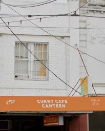 Orange storefront awning reading CURRY CAFE CANTEEN below a white brick building exterior with a window grille