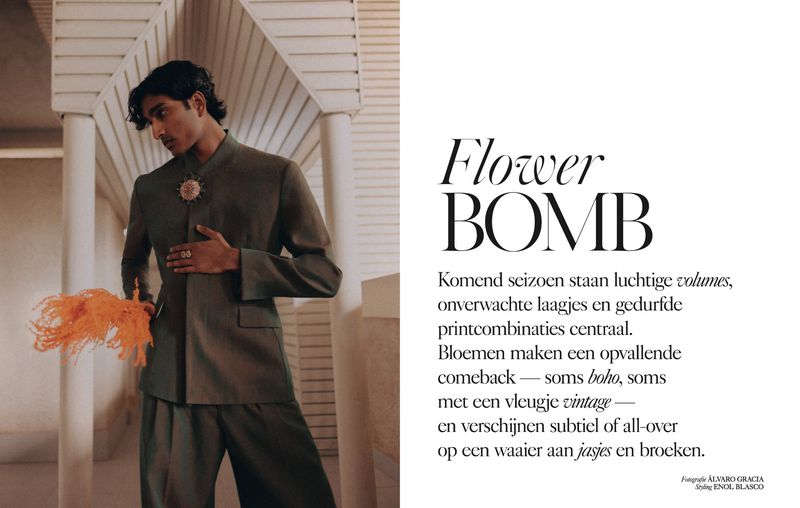 A male model in a green suit poses in front of white architectural details, holding an orange feather accessory, with magazine text in the background.