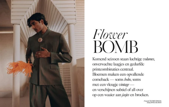 A male model in a green suit poses in front of white architectural details, holding an orange feather accessory, with magazine text in the background.