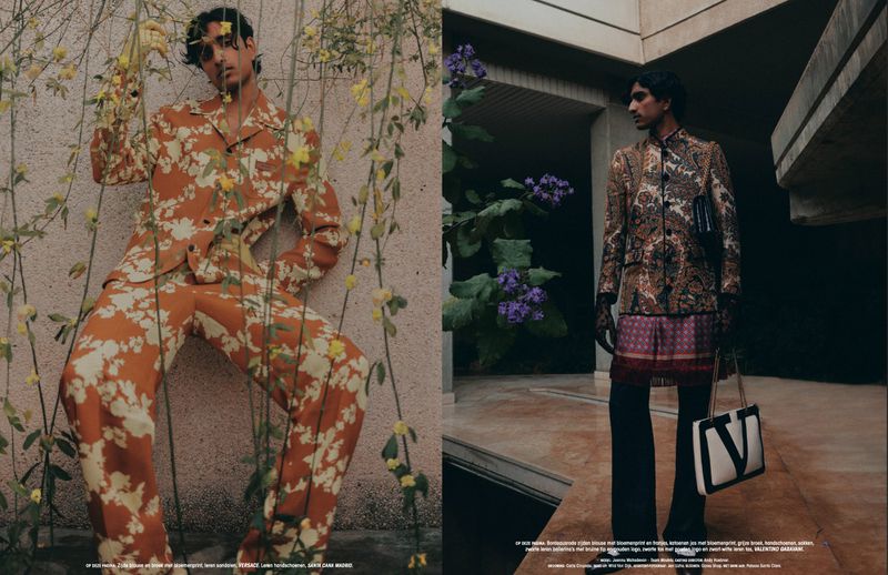 Editorial fashion shot of a man in a floral suit leaning against a wall with flowers, and another man in a paisley suit standing outside.