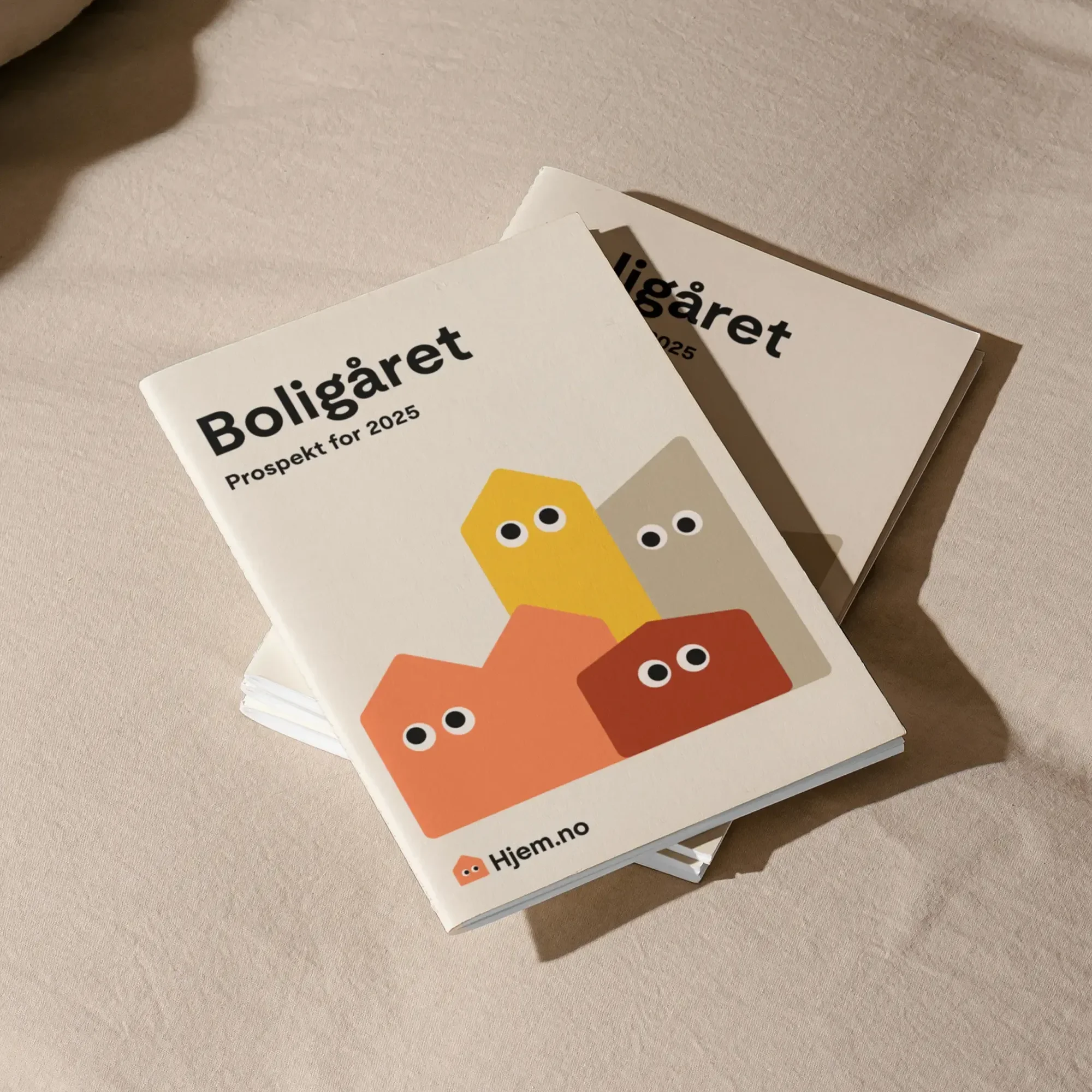 Two stacked Boligåret booklets, titled "Boligåret Prospekt for 2025," feature colorful, stylized house icons on a light background, casting soft shadows.