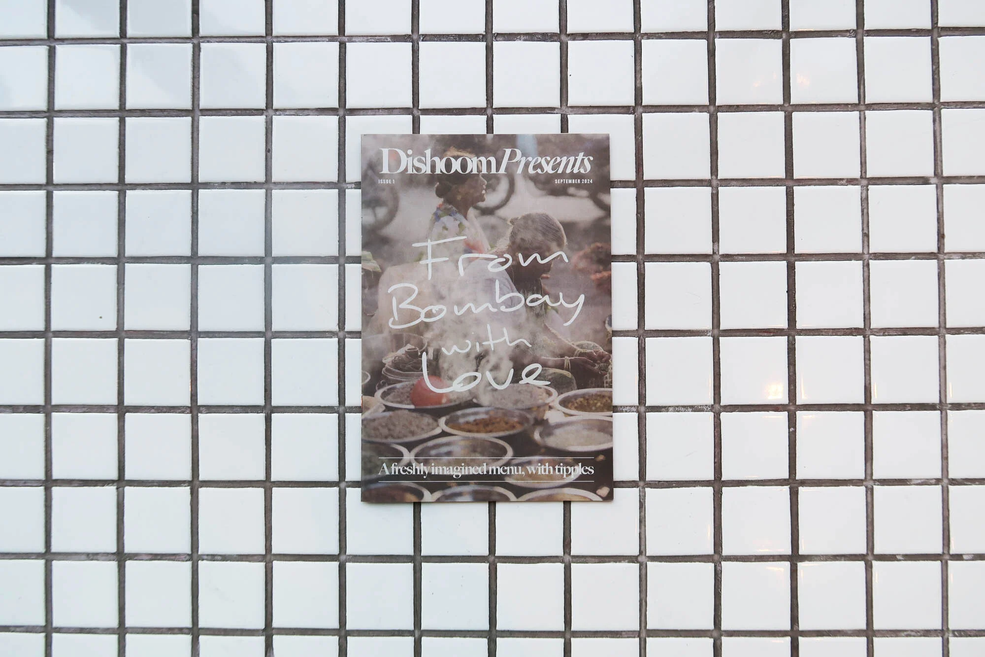 Dishoom Presents magazine cover featuring an image of Bombay street food and chefs on a white tiled wall in a portrait layout.