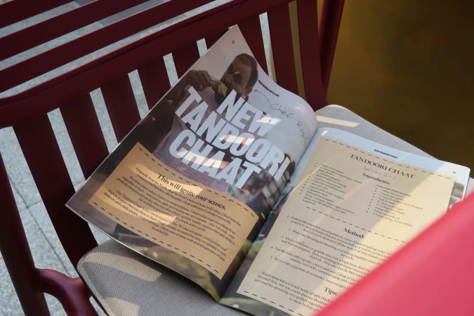 Open magazine on a red chair with a focus on Indian cuisine, showcasing a recipe for Tandoori Chaat with visible food imagery and text.