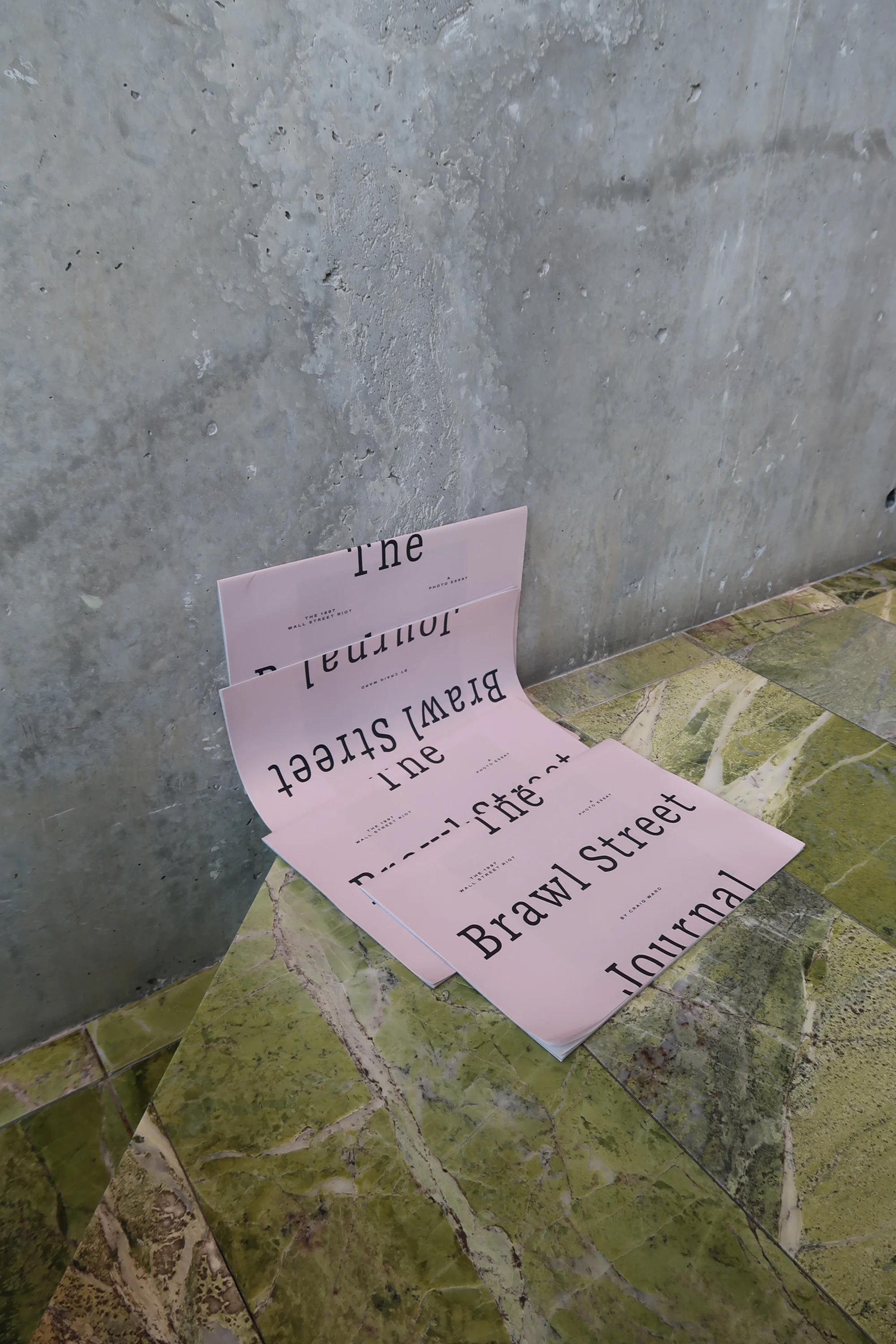 Close-up on three pink paper sheets with dark text, arranged on a green marble surface against a grey wall. Focus on typography.