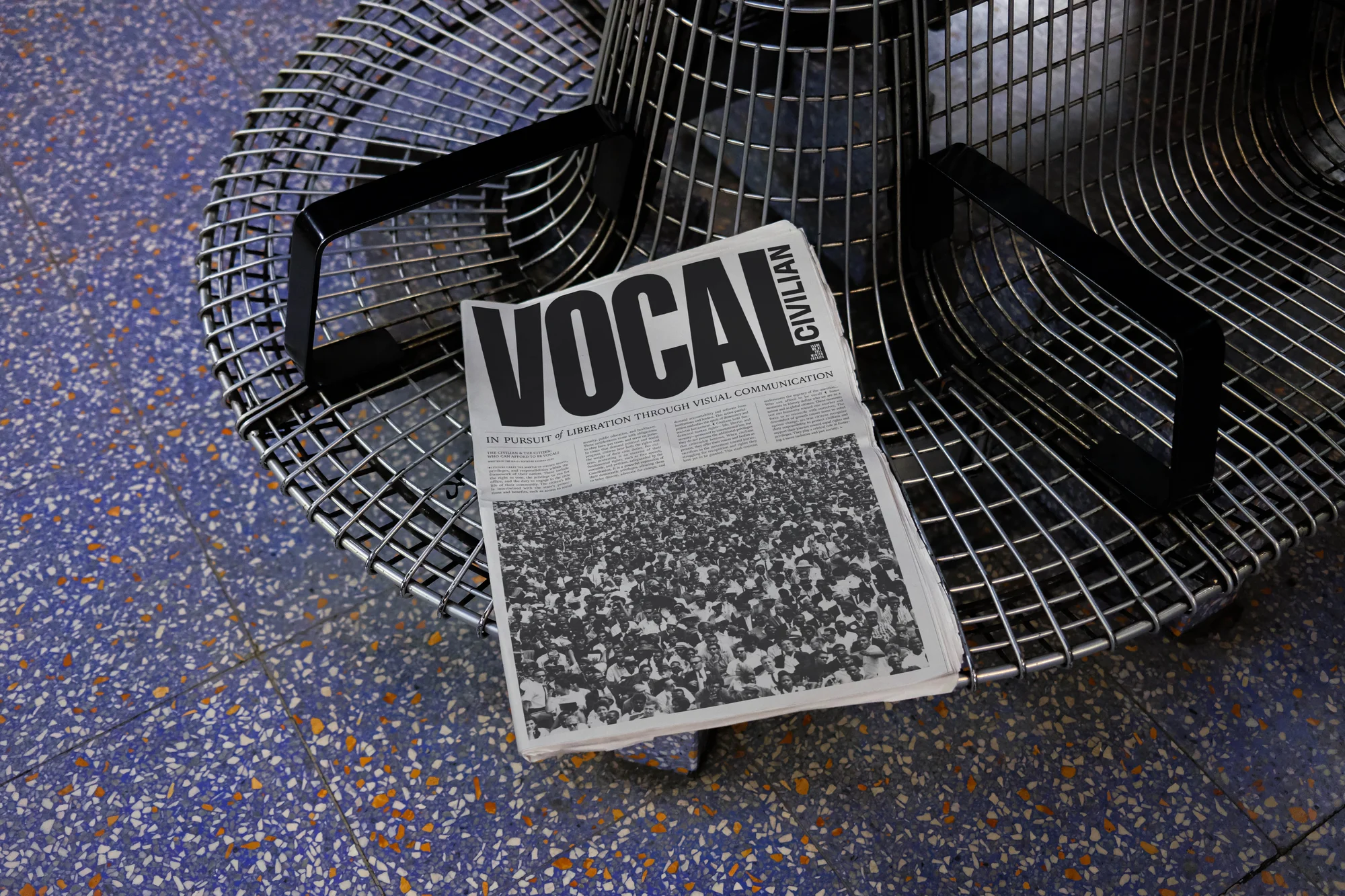 A newspaper titled 'Vocal Civilian' sits on a modern wire chair against a speckled blue and tan floor, capturing a study in contrasts.