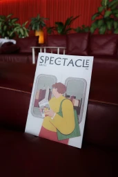 Printed magazine cover titled Spectacle featuring a graphic illustration of a person on public transport