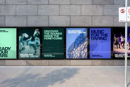 A series of advertising posters for Melbourne Recital Centre displayed on a gray stone tile wall in an outdoor public space.