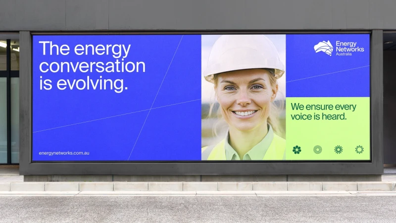 Outdoor billboard featuring a smiling construction worker alongside text promoting energy conservation and ensuring every voice is heard.
