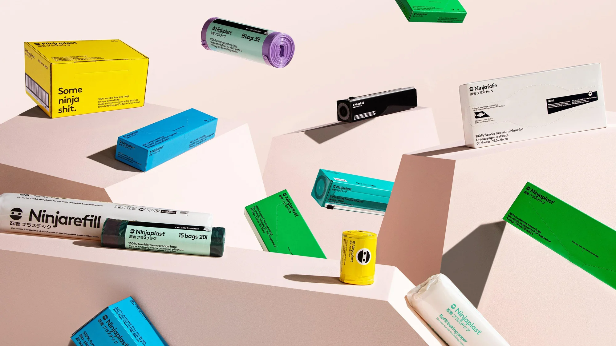 Still-life product shot of Ninjaplast-branded household products: garbage bags, tin foil, and refill baking paper in colorful packaging, elevated on a set.