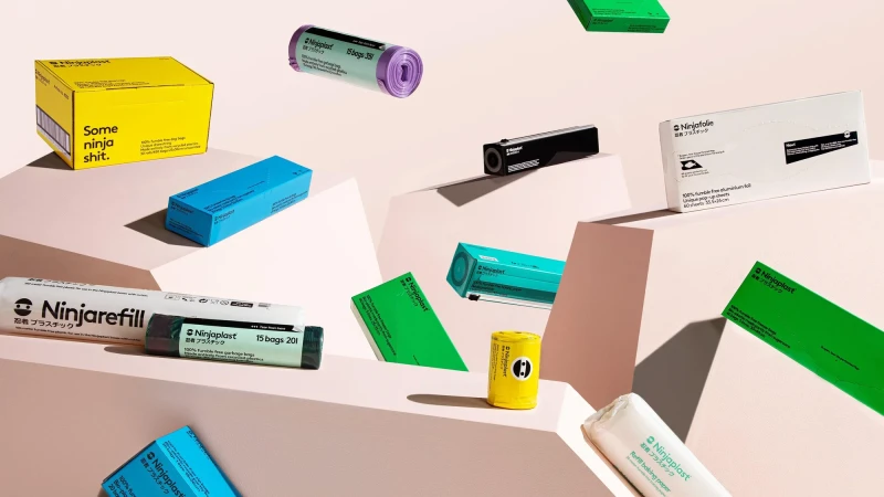 Still-life product shot of Ninjaplast-branded household products: garbage bags, tin foil, and refill baking paper in colorful packaging, elevated on a set.