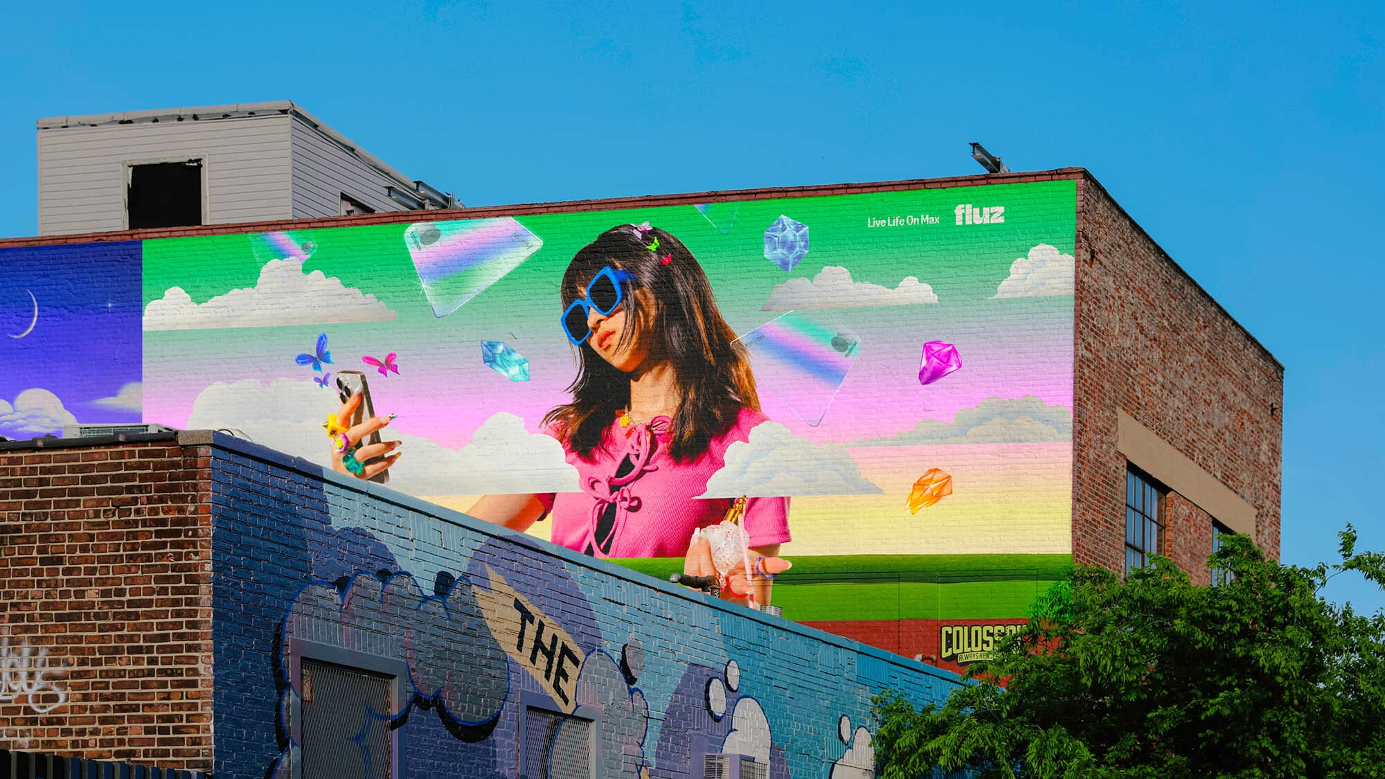Building mural of a woman in sunglasses holding a phone, with floating phone graphics and clouds, under a bright blue sky.