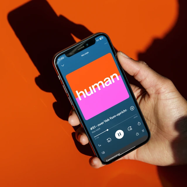 Hand holding a modern smartphone, displaying the Human app logo in a minimalist, colorful design, with a bright orange background.