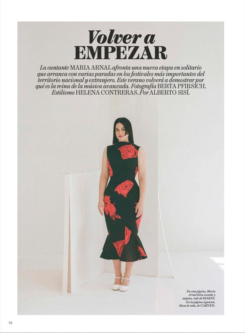 Portrait of Maria Arnal in a black floral dress, posing indoors in a magazine editorial shot. Fashion photography with neutral background.