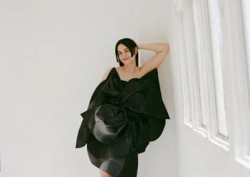 Woman in an oversized black sculptural dress leaning against a white wall with windows for Vogue Espana by Berta Pfirsich.