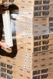 Person wrapping a large stack of cardboard boxes branded with Great Wrap in clear stretch film.
