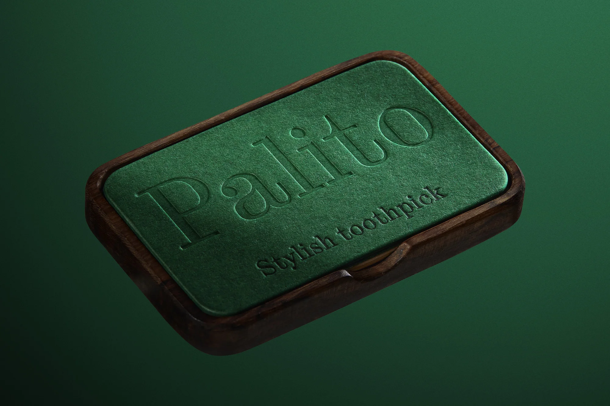 Close-up studio shot of a stylish wooden toothpick case with green felt insert and embossed lettering, set against a matching green backdrop.