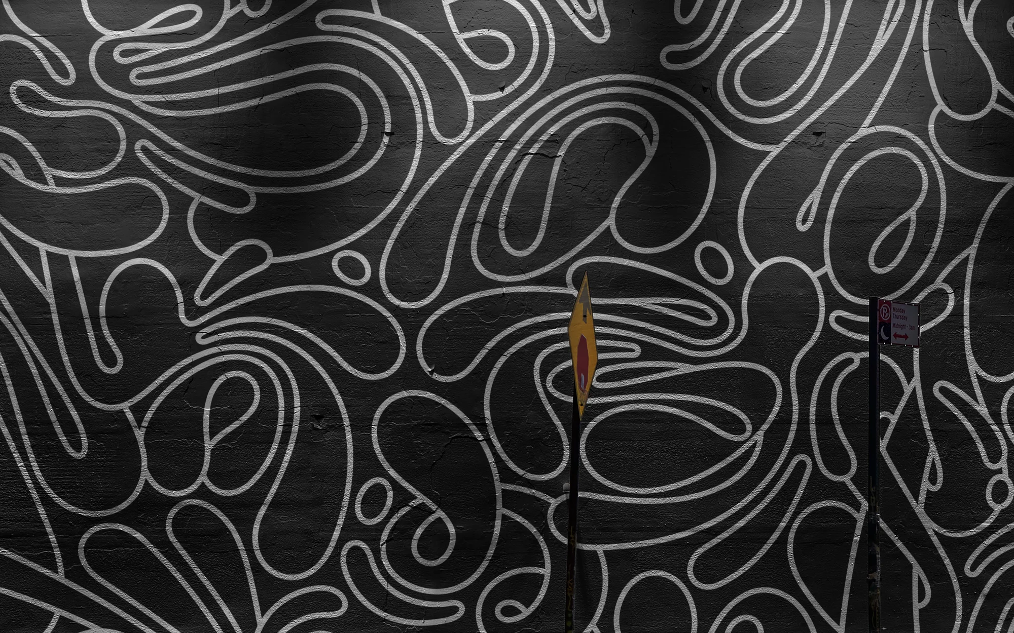 Abstract graffiti art on an outdoor concrete wall with looping lines and two small street signs in the urban environment.