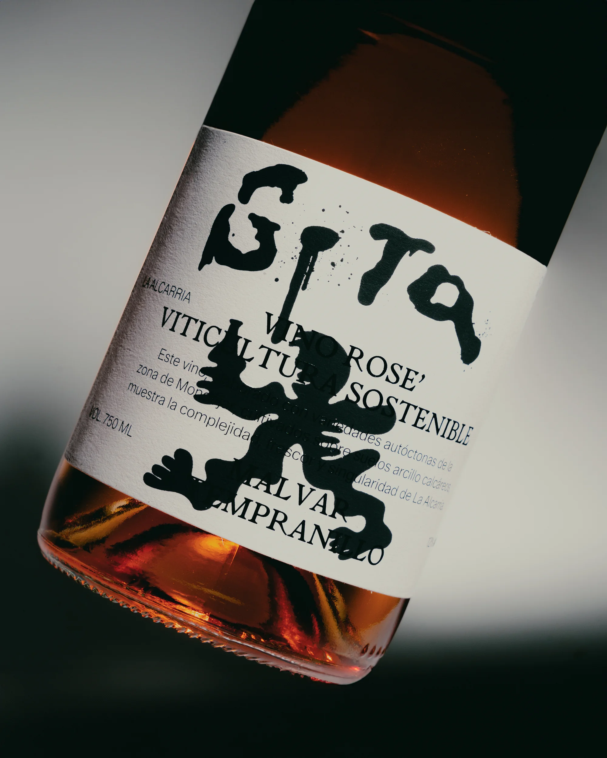 Wine bottle angled close-up on white background with a playful black graphic figure and bold, handwritten-style typography on the label.