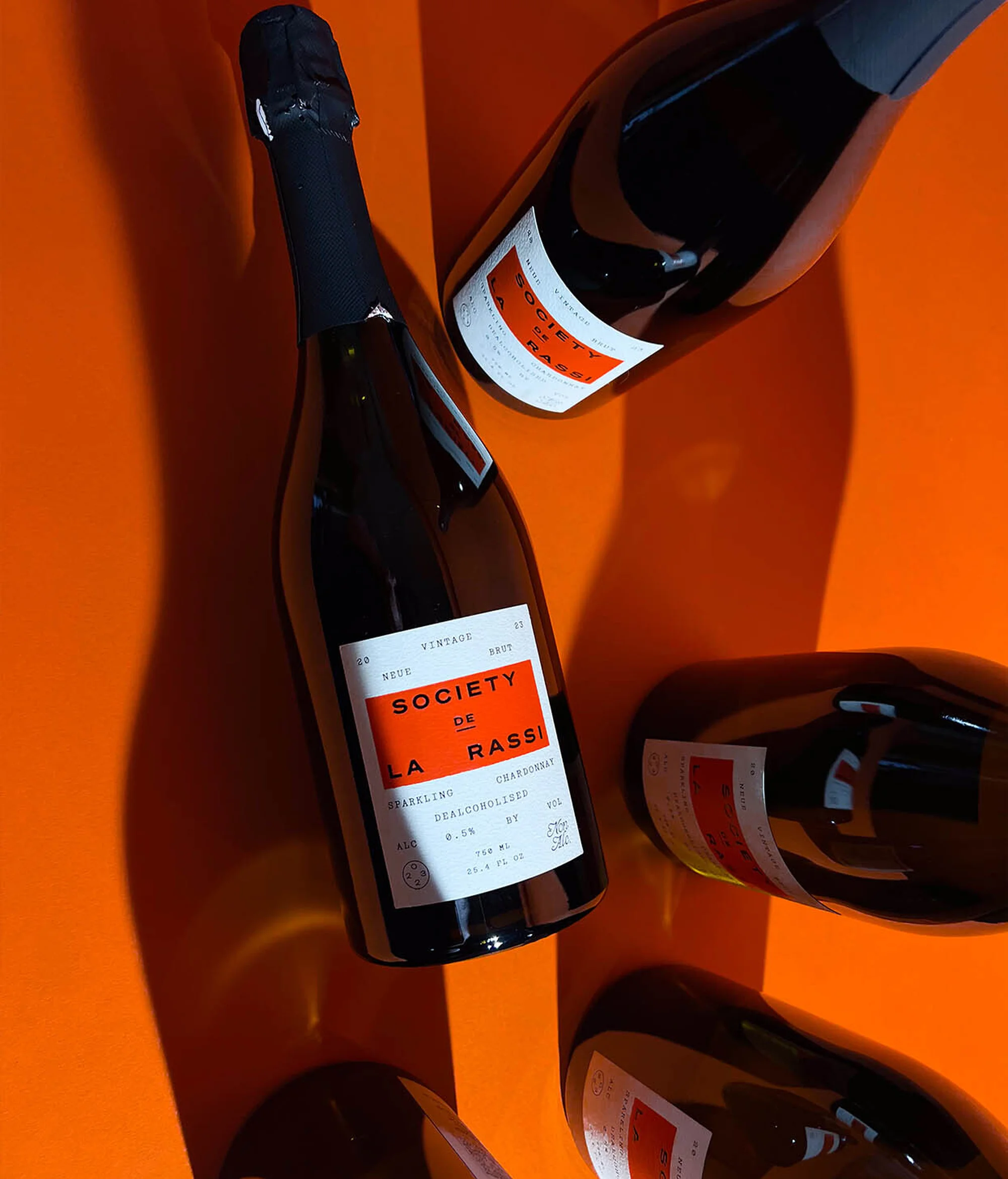 Overhead studio shot of several dark glass wine bottles on a bright orange surface with bold shadows and a clean, modern aesthetic.