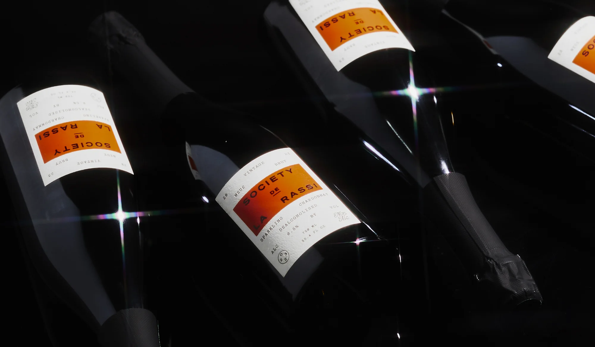 Several black wine bottles with white labels featuring an orange block and black text are displayed against a dark background.