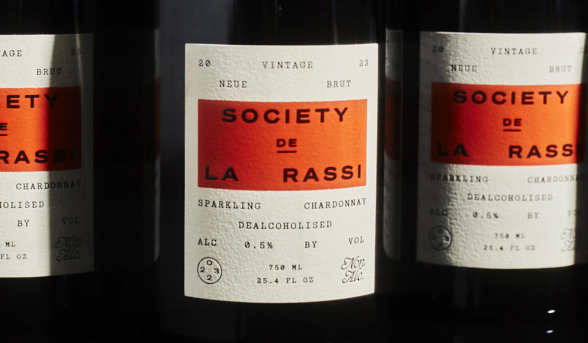 Three bottles of sparkling, dealcoholized Chardonnay 'Society de la Rassi' stand in a studio with a close-up perspective.