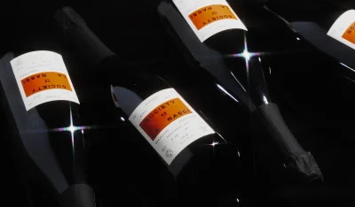 Four dark wine bottles with white and orange labels lying on a black reflective surface with star filter light flares.