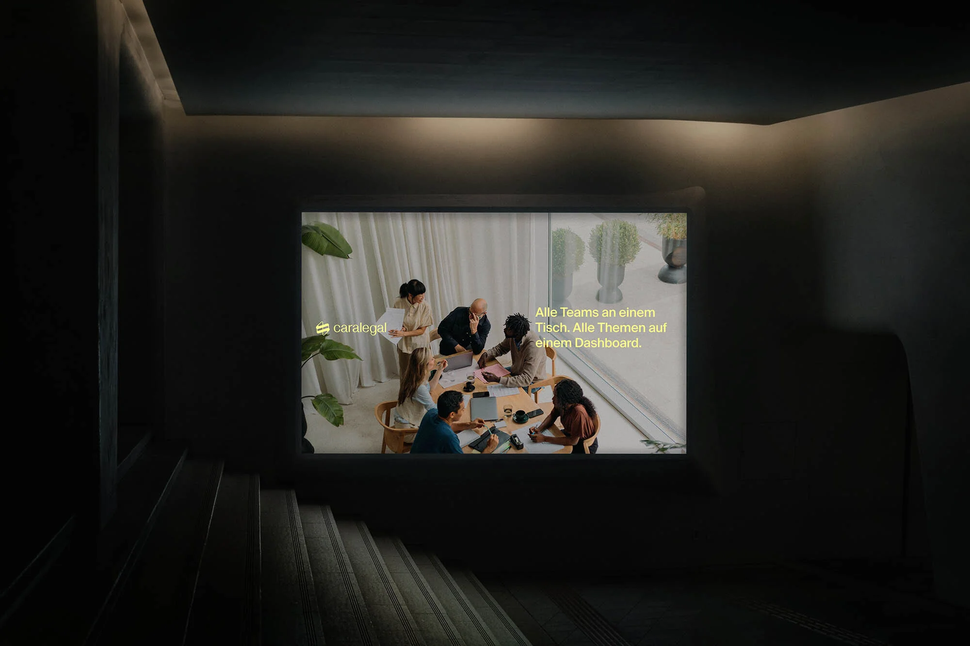 Office meeting scene projected in dark room. Diverse group of adults collaborates around a table, bright window behind them.  